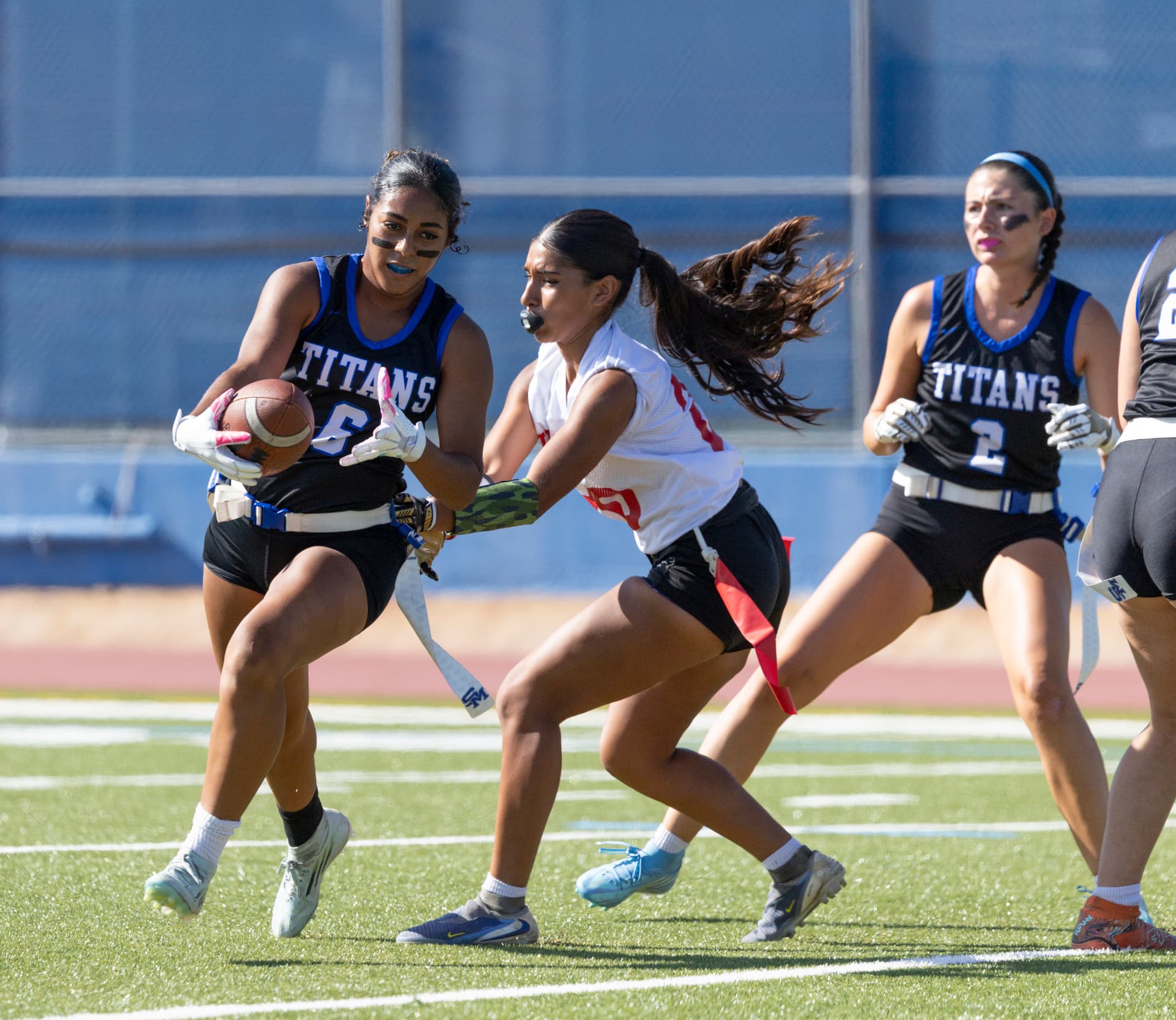 Titans No. 6 turns upfield with the football, fighting off a defender's flag pull as teammate No. 2 trails the play.