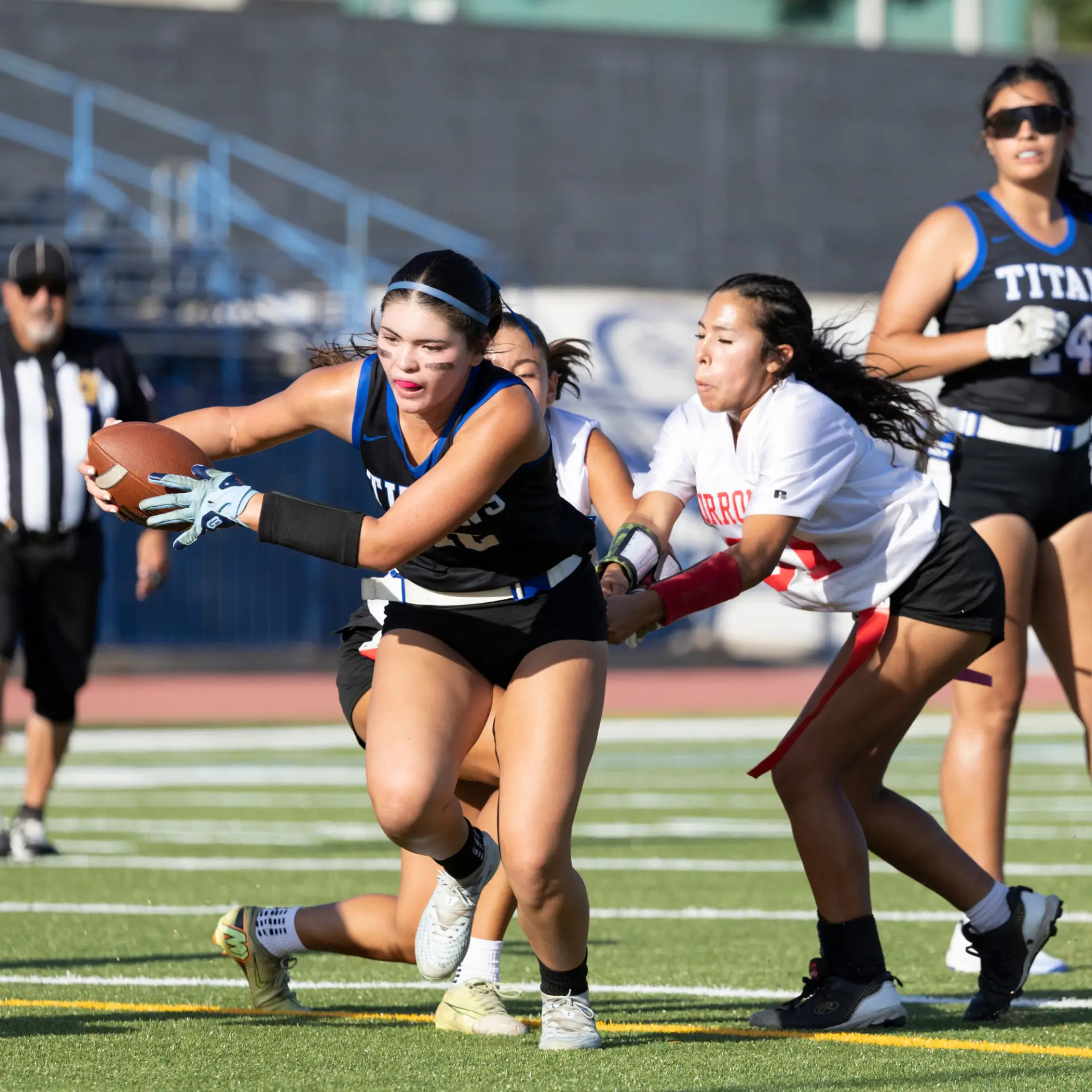 Player of the Game Kaia Kooper — a Titans ball carrier protects the football as a Burroughs defender closes in.