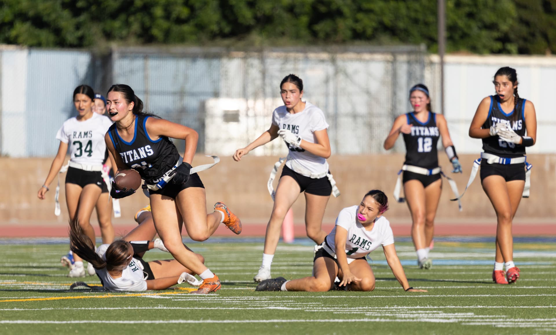 A Titans ball carrier runs past two defenders who dove and fell trying to pull her flags, with No. 12 running her route downfield.